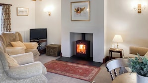 A cozy living room with a fireplace, comfortable seating, a television, and decorative wall art. - Attractive farm cottage with period features and views over fields and fells. (Caldbeck, near Keswick)