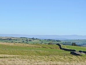 A rural landscape with rolling hills, a stone wall, and distant mountains under a clear sky.