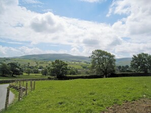 Un paysage rural caractérisé par des collines douces, un champ délimité par une clôture et une étendue d’eau.