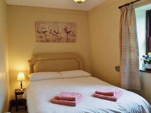 Un dormitorio con una cama, una mesita de noche con lámpara, un cuadro en la pared y una ventana con cortinas.