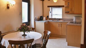 A kitchen with wooden cabinets, a countertop, a sink, and a dining area with a table and chairs. - Attractive farm cottage with period features and views over fields and fells. (Caldbeck, near Keswick)