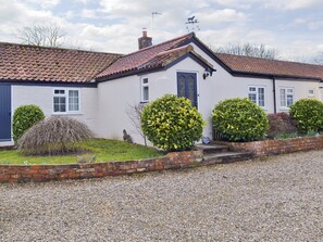 A two-story house with a red-tiled roof, white exterior walls, and a blue door. There are three well-maintained bushes in front of the house. - 3 bedroom accommodation in Foxholes, near Scarborough (Foxholes, near Scarborough)