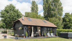 A wooden cabin with a sloped roof, a patio with outdoor seating, and a small garden area with potted plants. - 1 bedroom accommodation in White Colne, near Colchester (White Colne, near Colchester)