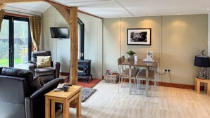 A modern living room with a fireplace, leather sofa, wooden coffee table, and a dining area with clear chairs. - 1 bedroom accommodation in White Colne, near Colchester (White Colne, near Colchester)