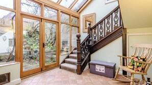A conservatory with large glass doors, a wooden staircase, a shoe & boot box, and a rocking chair. - 4 bedroom accommodation in Wells-next-the-Sea (Wells-next-the-Sea)