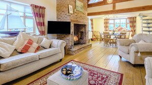 A cozy living room with a fireplace, wooden beams, a sofa, and a dining area. - 4 bedroom accommodation in Wells-next-the-Sea (Wells-next-the-Sea)