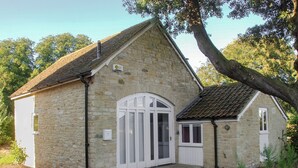 A stone building with a white door and window shutters, surrounded by greenery. - 1 bedroom accommodation in Fifehead Magdalen, near Gillingham (Fifehead Magdalen, near Gillingham)