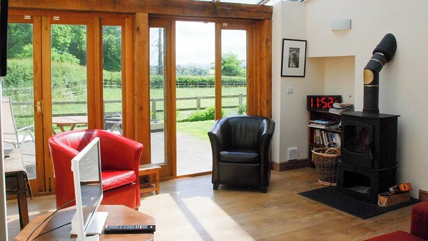 A living room with a glass ceiling, a fireplace, a red chair, a black chair, and a wooden table with a laptop. - 1 bedroom accommodation in Fifehead Magdalen, near Gillingham (Fifehead Magdalen, near Gillingham)