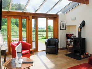 Una sala de estar con techo de vidrio, una chimenea, una silla roja, una silla negra y una mesa de madera con una computadora portátil.