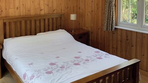 A wooden paneled room with a bed, a bedside table with a lamp, and a window with curtains. - 1 bedroom accommodation in Burgate, near Fordingbridge (Burgate, near Fordingbridge)