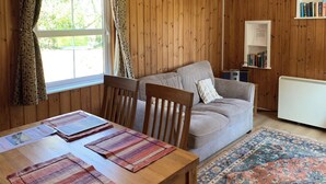 A wooden-paneled room with a sofa, a dining table with placemats, a bookshelf, and a radiator. - 1 bedroom accommodation in Burgate, near Fordingbridge (Burgate, near Fordingbridge)