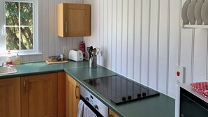 A kitchen with wooden cabinets, a built-in oven, a stovetop, and a window with a view of trees. - 1 bedroom accommodation in Burgate, near Fordingbridge (Burgate, near Fordingbridge)