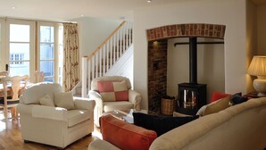 A living room with a fireplace, a staircase, and a dining area with chairs. - 3 bedroom accommodation in Chulmleigh, near South Molton (Chulmleigh, near South Molton)