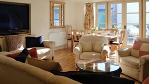 A living room with a television, sofas, a glass coffee table, a dining area with chairs, and large windows. - 3 bedroom accommodation in Chulmleigh, near South Molton (Chulmleigh, near South Molton)