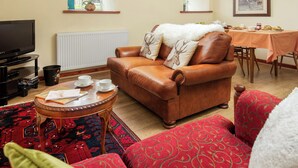 Ein Wohnzimmer mit braunem Ledersofa, einem roten Couchgarnitur, einem Couchtisch, einem Fernseher und einem Essbereich mit Tisch und Stühlen.