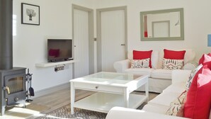 A living room with a white sofa, a coffee table, a TV on a shelf, and a fireplace. - Wishing Well Cottage (Mathon, near Malvern)