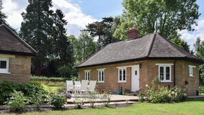 A stone cottage with a tiled roof, a small garden with a patio table and chairs, and a lawn. - Wishing Well Cottage (Mathon, near Malvern)