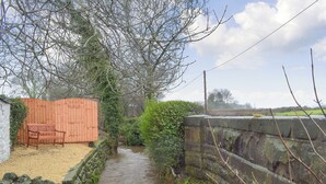 A narrow stream flowing through a rural area with a wooden fence and a stone wall on one side.
