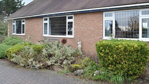 Een twee verdiepingen tellend bakstenen huis met een pannendak, grote ramen en een tuin met diverse planten en een beeld.