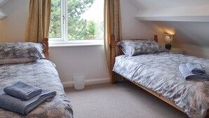 Een slaapkamer met twee eenpersoonsbedden, een raam met gordijnen, een bedlampje en een kleine prullenbak.