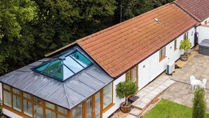 A two-story house with a sloped roof, a skylight on the upper floor, and a small garden with a lawn and a tree. - 1 bedroom accommodation in Boughton, near Downham Market (Boughton, near Downham Market)