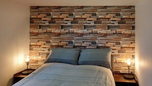 Een bed met een hoofdbord van verschillende houten planken, twee bedlampen en een sprei.