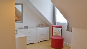 Ein Schlafzimmer mit einem weißen Kommoden, einem roten Hocker, einem Spiegel und einer Deckenleuchte.