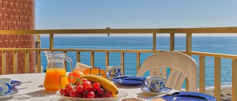A table set with breakfast items including bread, fruit, and juice, overlooking the sea.