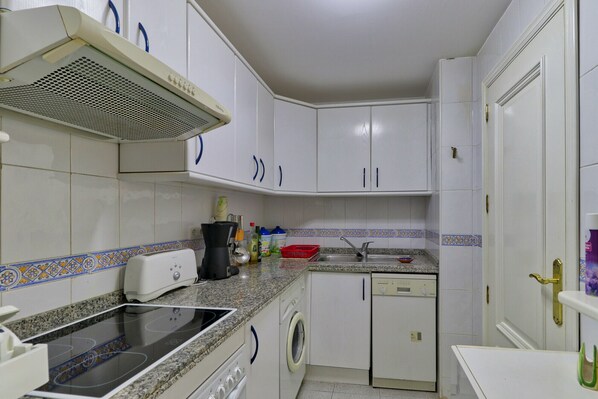 Una cocina compacta con armarios blancos, una estufa integrada, una lavadora y un lavamanos.