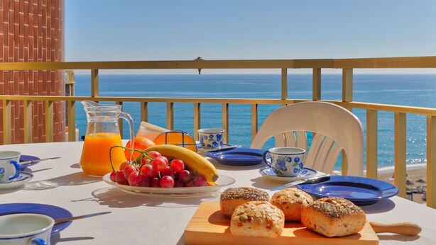 Ein Tisch mit Frühstücksgebäck, Trauben und einer Banane, mit Blick auf das klare, blaue Meer.
