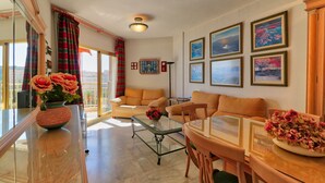 Ein geräumiges Wohnzimmer mit Balkon, einer Sofagarnitur, einem Couchtisch und einem Esstisch.