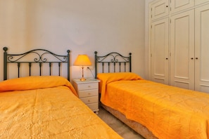 A bedroom with two single beds, a nightstand with a lamp, and a wardrobe.