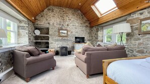 Une pièce chaleureuse avec des murs en pierre, un plafond en bois, deux canapés, un lit, une télévision et une fenêtre.