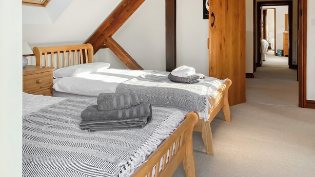 Une chambre avec deux lits, une lucarne, des poutres en bois, un couloir et une porte.