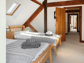 A bedroom with two beds, a skylight, wooden beams, a hallway, and a door.