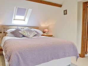 A bedroom with a bed, pillows, a bedside lamp, a window, and a wooden ceiling beam. - The Granary - W43949 (East Tytherton, Chippenham)