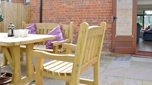 A wooden table and chairs outside a brick building with a door leading to an interior space. - The Granary - W43949 (East Tytherton, Chippenham)