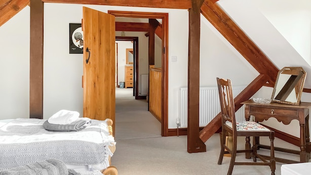 A bedroom with a bed, a wooden chair, a dresser, and a door leading to another room. - The Granary - W43949 (East Tytherton, Chippenham)
