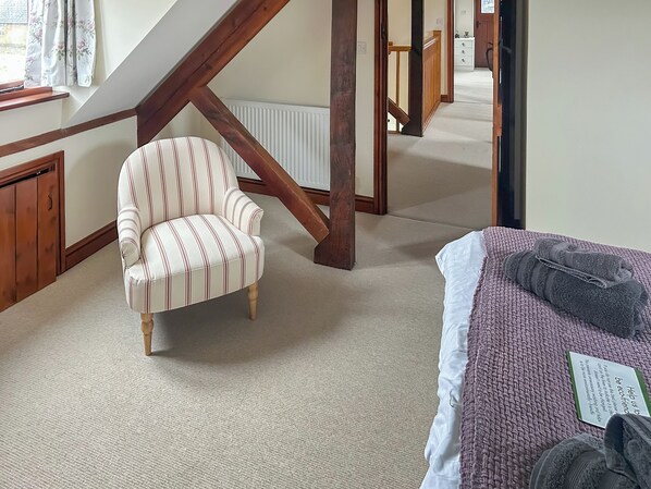 Una habitació amb una butaca estriada, un llit amb una manta amb textura, una escala de fusta i un radiador.