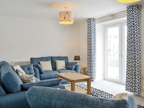 Un salon moderne avec un canapé bleu, une table basse en bois, des coussins à motifs, une lampe sur pied et un rideau à motifs.