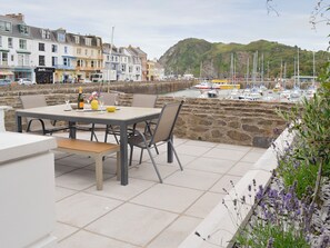 Een terras met een eettafel, uitkijkend op een haven met boten en een heuvel in de verte.