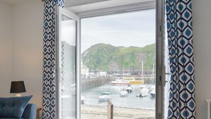 A room with a large window offering a view of a harbor with boats and a hilly landscape. - 3 bedroom accommodation in Ilfracombe (Ilfracombe)