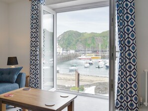 Een kamer met een groot raam dat uitzicht biedt op een haven met boten en een heuvellandschap.