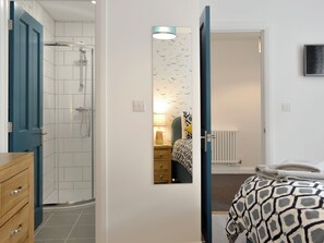 Une chambre à coucher comprenant un lit, une table de chevet et un miroir, ainsi qu’une salle de bain avec douche.
