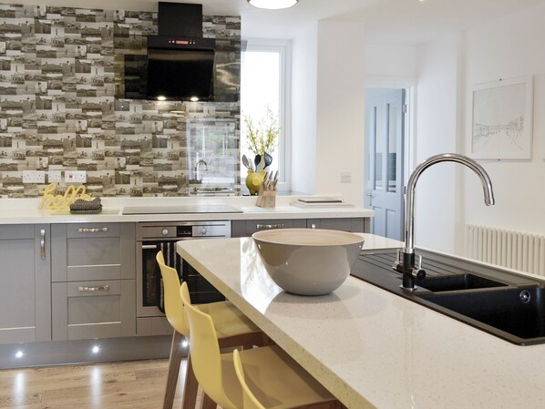 Een moderne keuken met een groot eiland, roestvrijstalen apparatuur en een opvallende mozaïekachterwand.