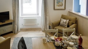 A living room with a sofa, a television, a dining table set with plates, cups, and a bottle, and a window with curtains. - 3 bedroom accommodation in Ilfracombe (Ilfracombe)
