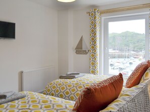 A bedroom with a bed, a window with a view of boats, a mounted TV, and a radiator.