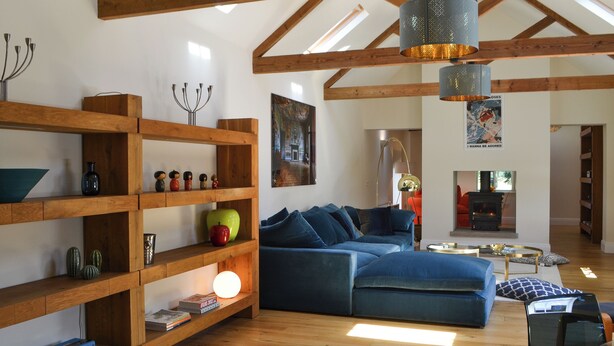 A spacious living area with wooden beams, a blue sofa, a bookshelf, and a fireplace.