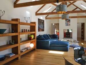 Ein geräumiger Wohnbereich mit Holzbalken, einem blauen Sofa, einem Bücherregal und einem Kamin.