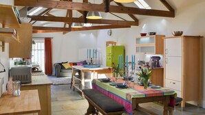 A rustic kitchen with exposed beams, a dining table set for six, and a green refrigerator.
